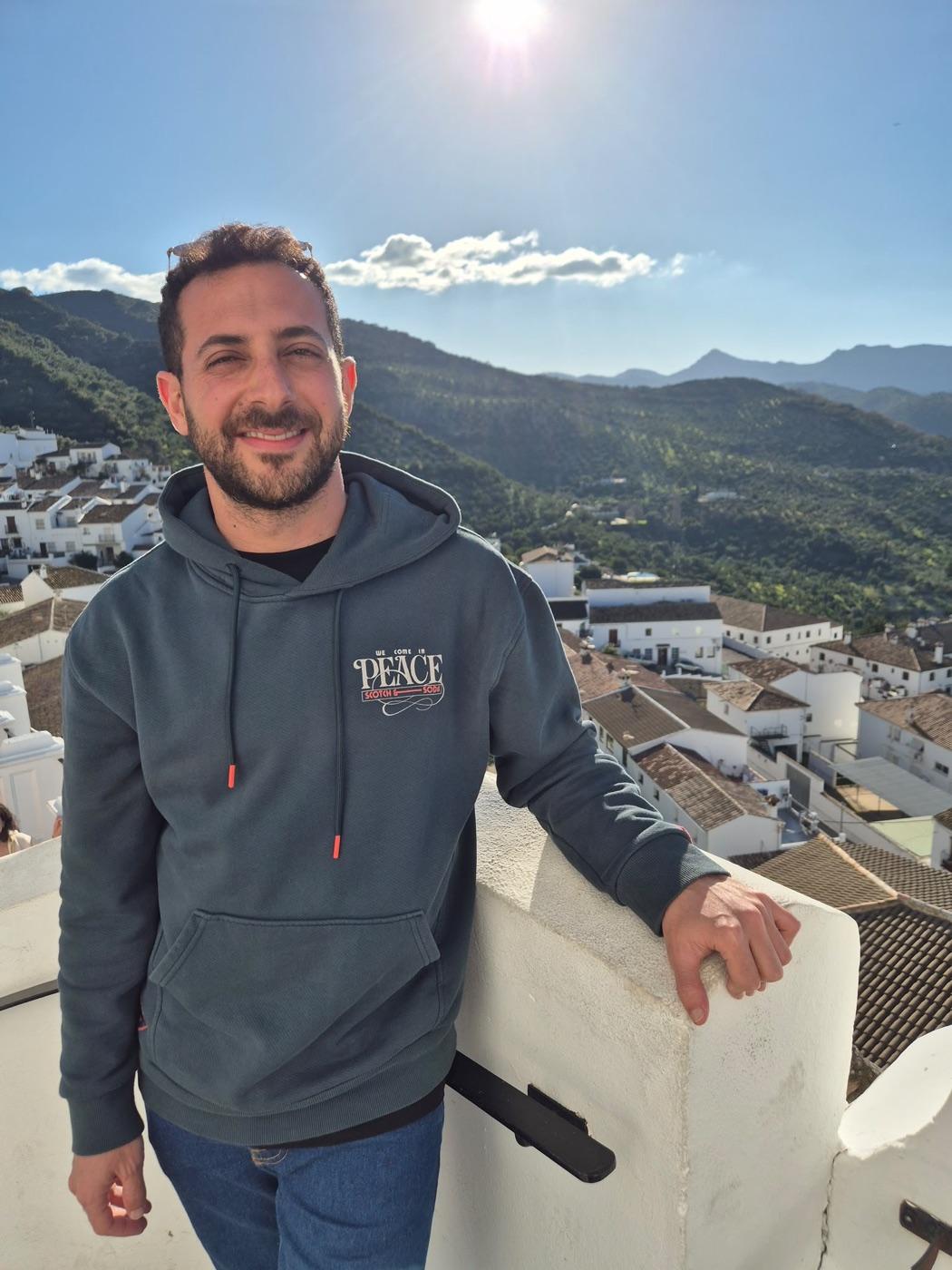 Gilad Wein smiling on a rooftop above a white village and green mountains